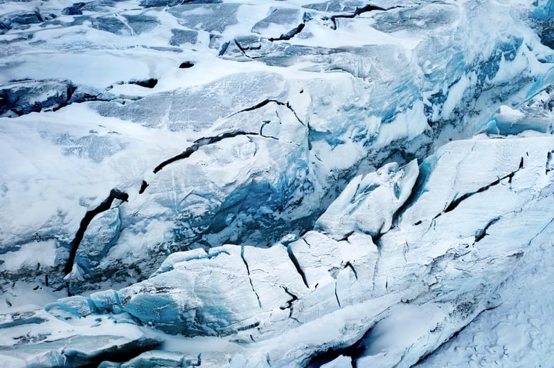 A landscape photo showing a glacier - black cracks are visible on the ice, and snow covers it in spots