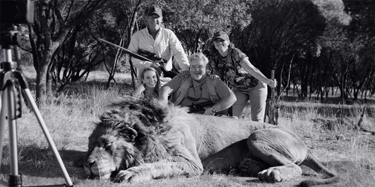 A black and white image of a dead lion, with a group of trophy hunters posing. This is a CGI artwork and no animals were hurt.