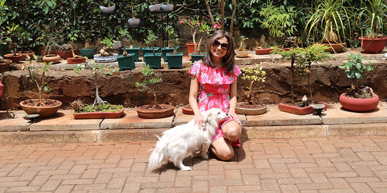 Award-winning writer Binny Shah-Patel kneeling on the ground, petting a fluffy white dog. She is wearing a pink dress and she