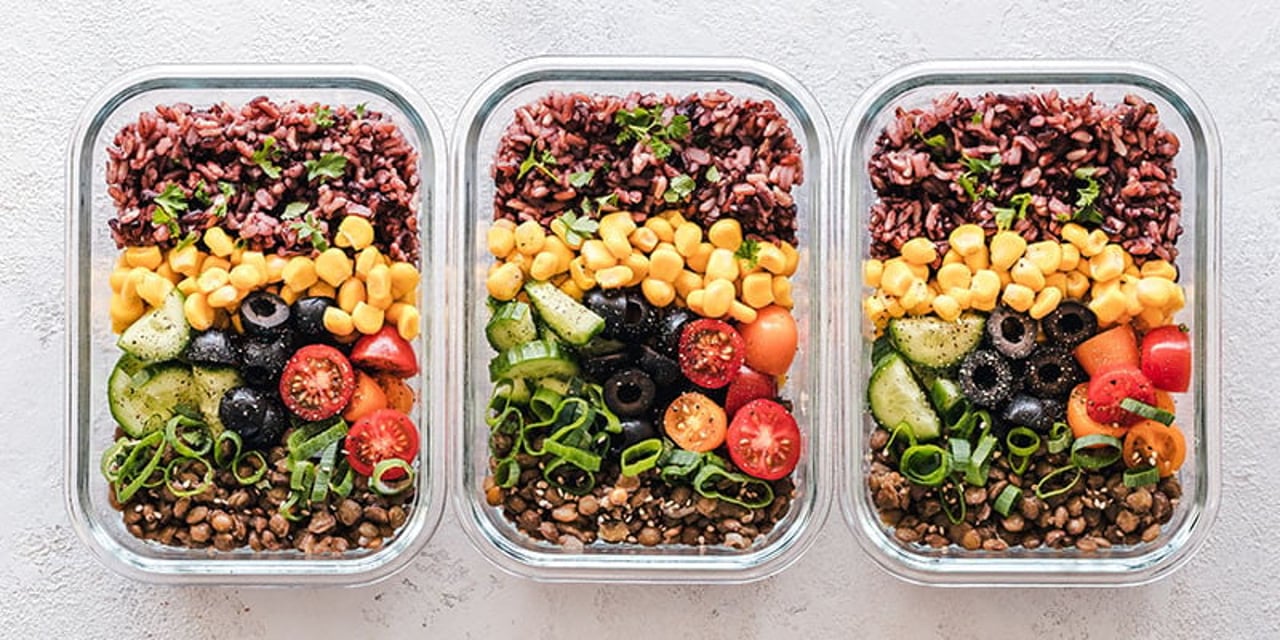 A row of 3 food containers with a variety of leftover foods in them