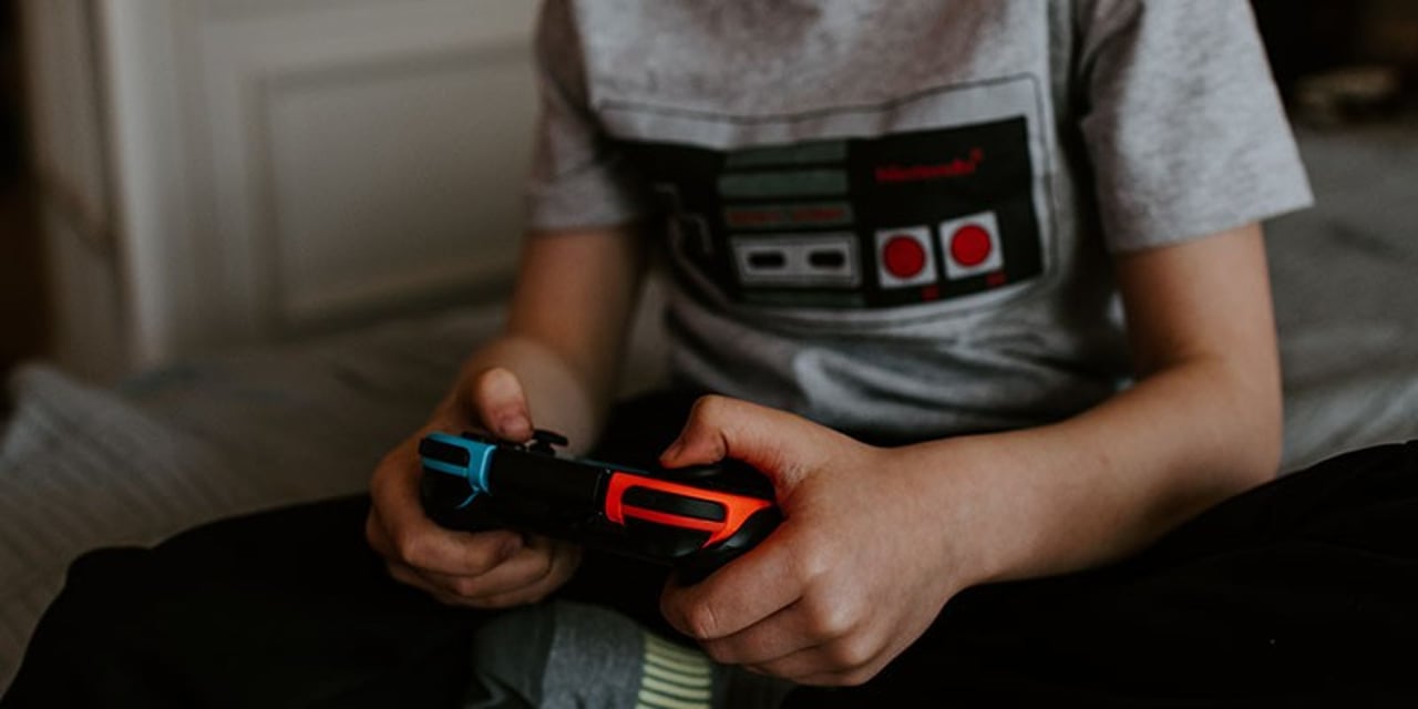 A person holds a Nintendo Switch gaming joystick, while wearing a t-shirt depicting an old-school N64 controller