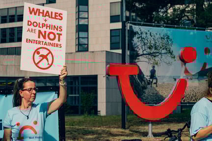 A protestor is holding up a sign that reads whales and dolphins are not entertainers. She is standing next to the TUI logo outside of their head offices in Hannover, Germany.