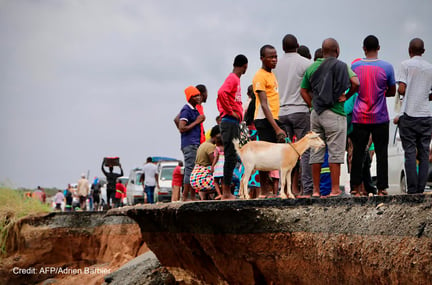 Locals stand beside a damaged section of the road with a goat after Cyclone Idai