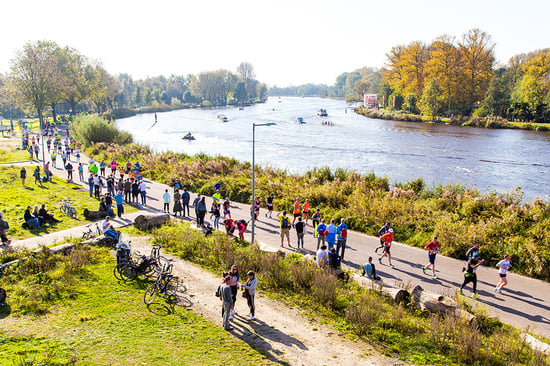 A group of people running along a scenic path beside the Amstel River in Amsterdam, surrounded by greenery and natural beauty.