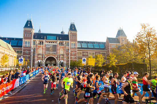 Runners participate in a marathon outside the Rijksmuseum in Amsterdam on a clear day, with banners and spectators lining the route.