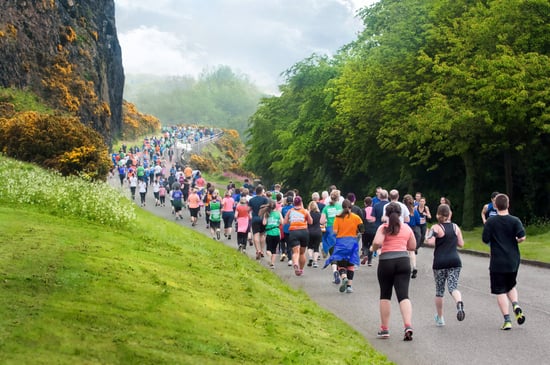 A group of runners running in a park with lush greenery around them.