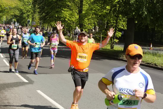 A lively scene of runners in a marathon, with one participant in an orange shirt raising their hands in excitement.