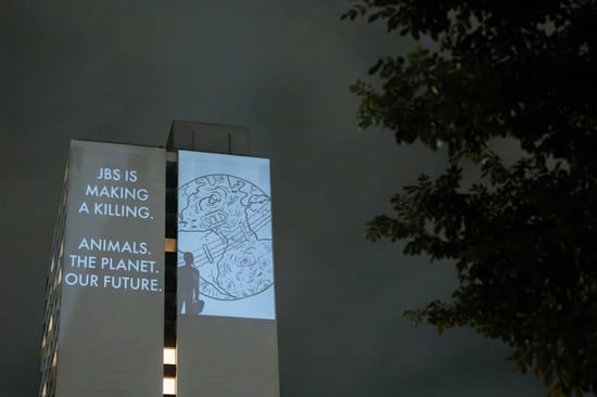 Projection on the side of a tower block saying 'JBS is making a killing. Animals. The Planet. Our future.