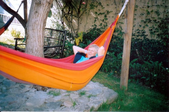Woman laying in an orange and pink hammock, arms behind her head and smiling at the camera.
