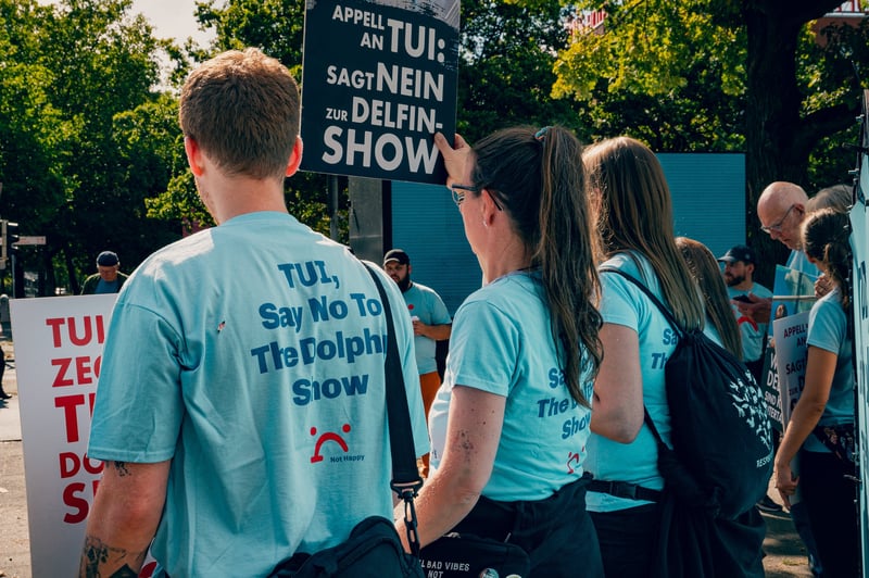 Protestors are holding up signs that to protest dolphin and whale captivity. They are wearing blue t-shirts reading TUI say no to the dolphin show